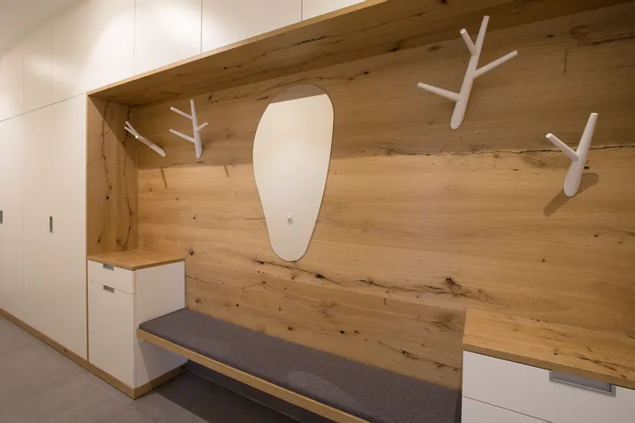 Moderner Garderobenbereich mit Holzverkleidung, weißen Haken und Sitzbank