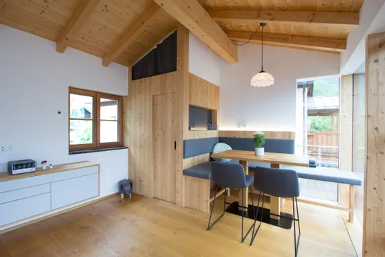 Moderne Wohnküche mit Holzwänden, Essbank, grauen Stühlen und Deckenlampe im Alpenstil