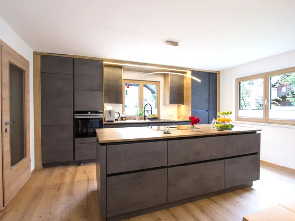 Moderne Einbauküche mit Kochinsel, grauen Fronten und Holzdetails bei Tageslicht