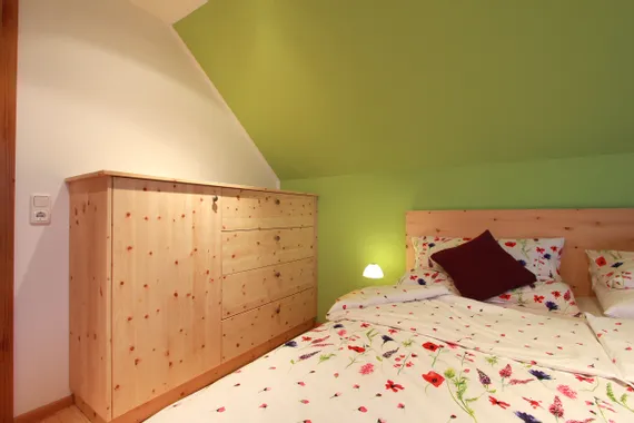 Gemütliches Schlafzimmer mit Blumenbettwäsche, grün gestrichener Wand und Möbeln aus hellem Holz