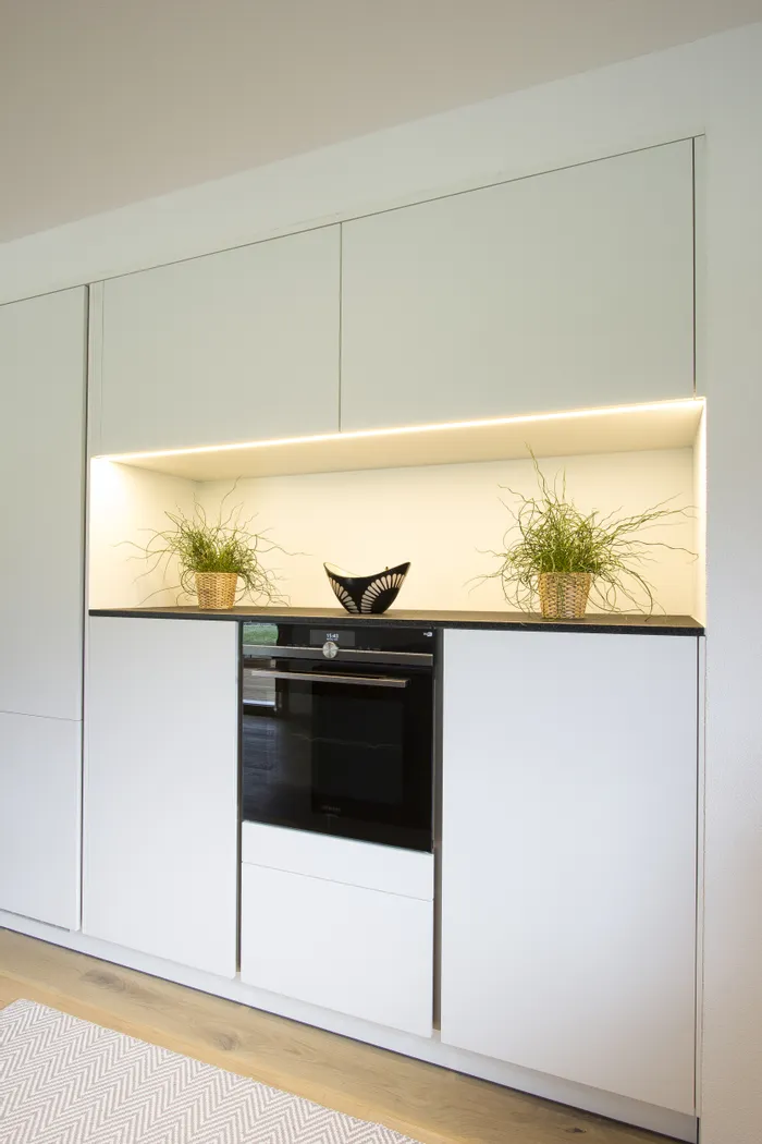 Moderne Einbauküche mit weißem Schrank, integriertem Backofen und Deko-Pflanzen