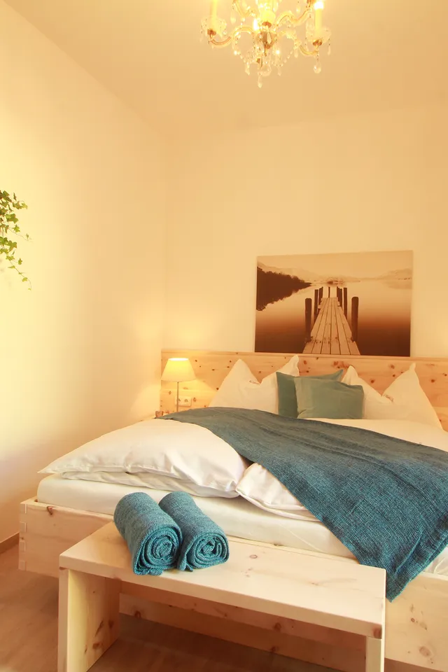 Helles Schlafzimmer mit Holzbett, blauer Decke, Nachttischen und Regalwand