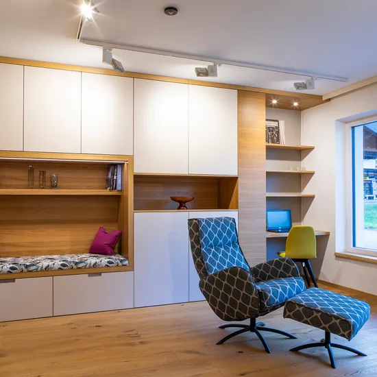 Modernes Wohnzimmer mit Einbauschränken, Lesesessel und großem Fenster mit Blick aufs Dorf