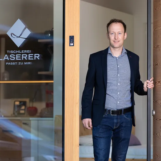 Geschäftsmann steht in geöffneter Holztür der Tischlerei Laserer
