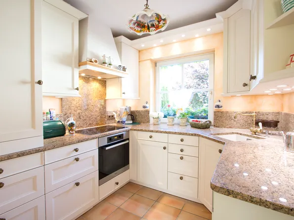 Landhausküche klasisch mit Granit-Arbeitsplatten, weißen Schränken und Blick auf Garten durch Fenster