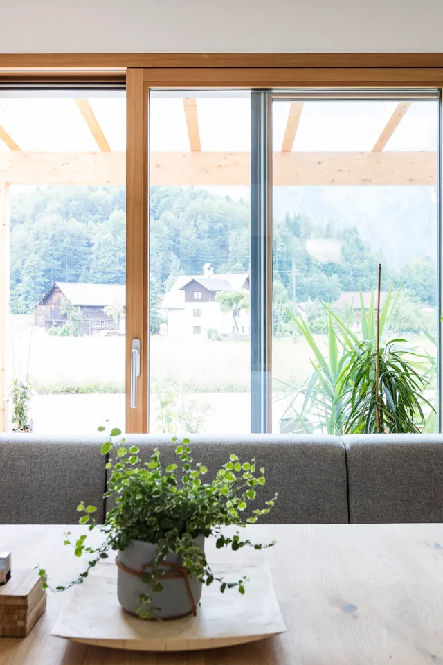 Helles Wohnzimmer mit Holztisch, Zimmerpflanzen und Blick auf die Berge durch große Panoramafenster