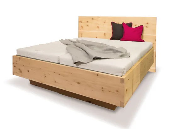 Massivholzbett aus Zirbenholz mit grauer Decke und passenden Zierkissen