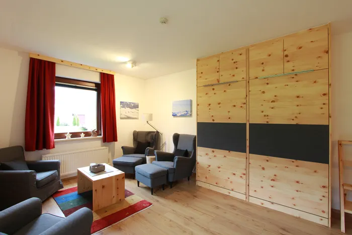 Gemütliches Wohnzimmer mit roten Vorhängen, grauen Sesseln und Holzmöbeln im Alpenstil