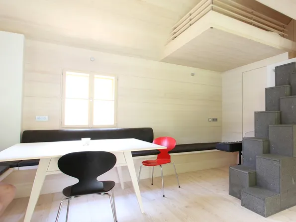 Helles minimalistisches Wohnzimmer mit Holzverkleidung, Esstisch, modernen Stühlen und grauem Treppenofen