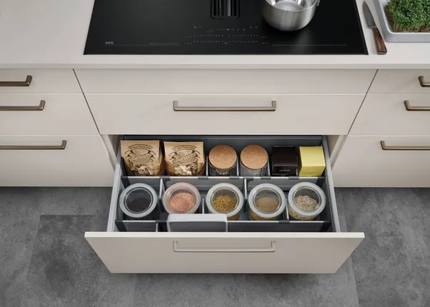 Offene Küchenschublade mit ordentlich sortierten Gläsern, Gewürzen und Vorräten in Trennfächern