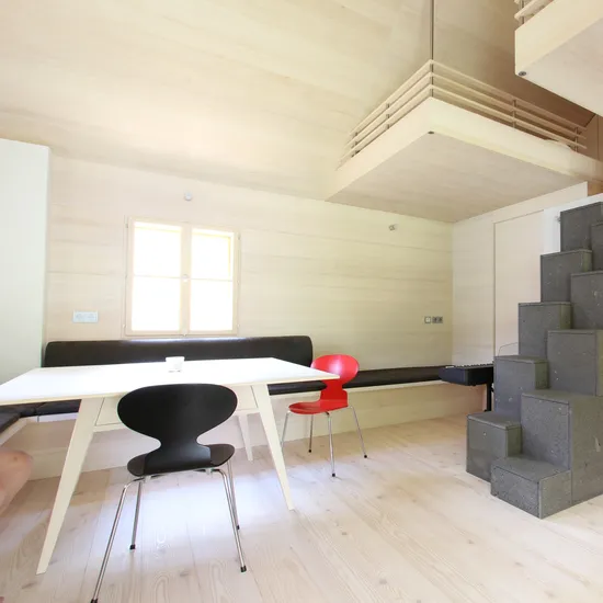 Helles minimalistisches Wohnzimmer mit Holzverkleidung, Esstisch, modernen Stühlen und grauem Treppenofen