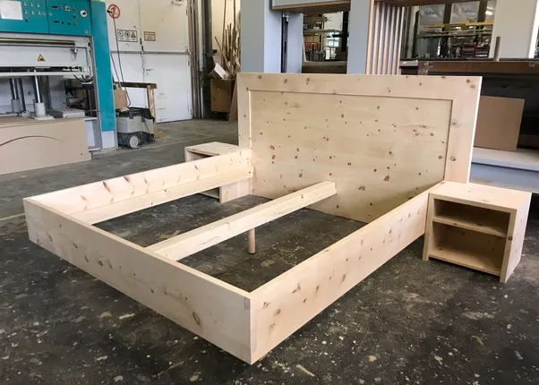 Unmontiertes Massivholzbett mit Kopfteil und Nachttisch in einer Schreinerei