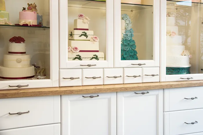 Ausstellung mit kunstvoll dekorierten Hochzeitstorten in einer Vitrine mit weißen Schränken