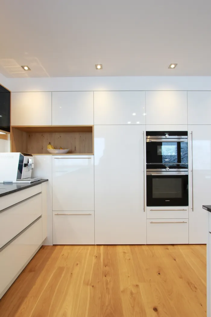 Moderne weiße Einbauküche mit Hochglanzfronten, Holzdetails und integriertem Backofen