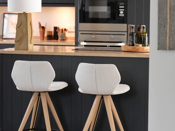 Moderne Küche mit zwei hellen Barhockern vor dunkler Kücheninsel und eingebautem Ofen