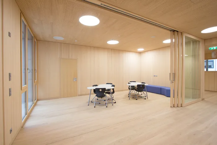 Moderner Klassenraum mit Holzwänden, runden Tischen und schwarzen Stühlen