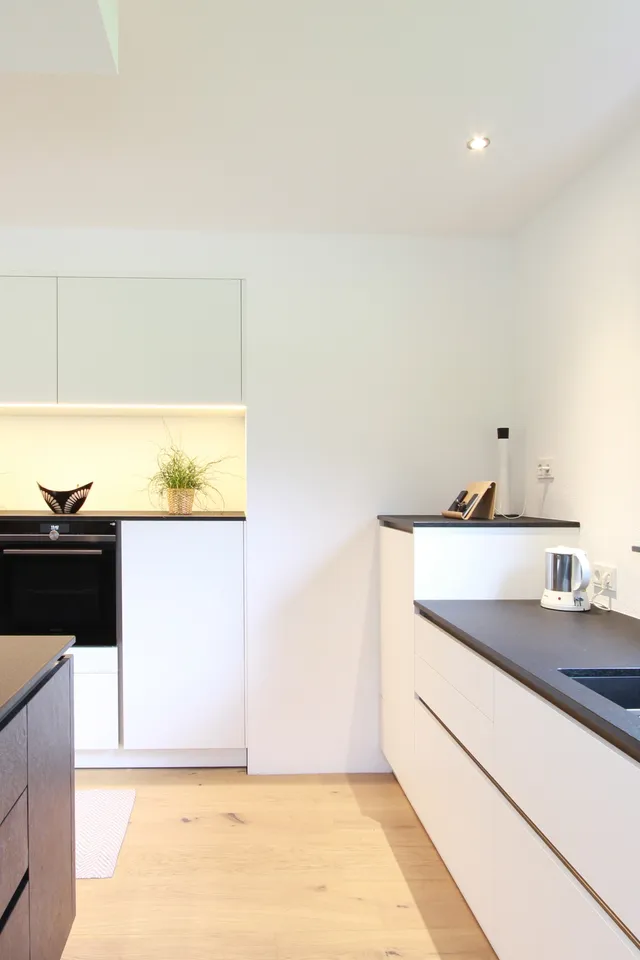 Moderne weiße Einbauküche mit schwarzer Arbeitsplatte und großem Fenster