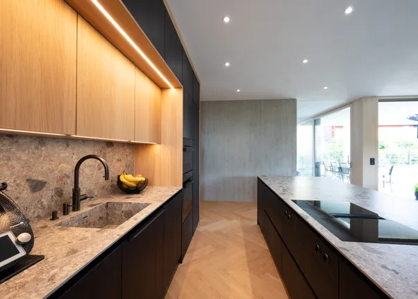 Moderne offene Küche mit dunklen Schränken, Steinplatte und eingebautem Induktionskochfeld