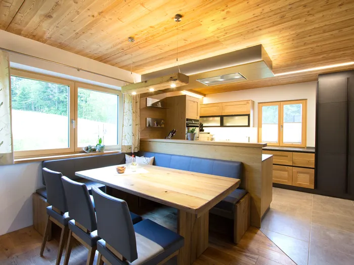 Moderne Wohnküche mit Holzdecke, Eckbank, Essbereich und Naturblick durch große Fenster