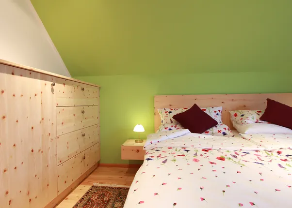 Gemütliches Schlafzimmer mit Holzbettrahmen, grüner Wandfarbe und floraler Bettwäsche