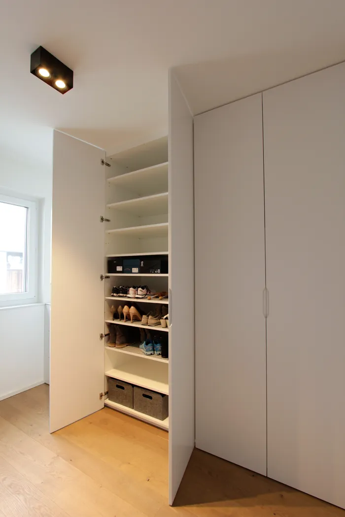 Geöffneter weißer Einbauschrank mit Regalen für Schuhe und Aufbewahrungsboxen