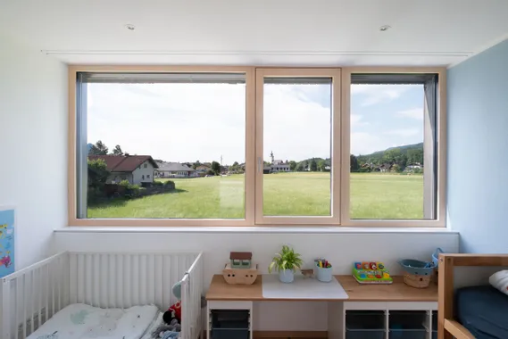 Kinderzimmer mit großem Fenster und Blick auf grüne Wiese und Dorfhäuser
