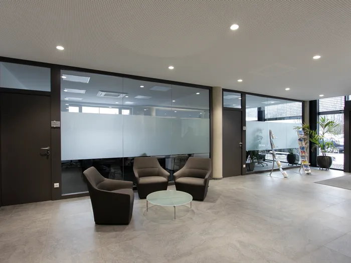Modern eingerichteter Eingangsbereich mit Glastüren, Loungestühlen und Infoständer
