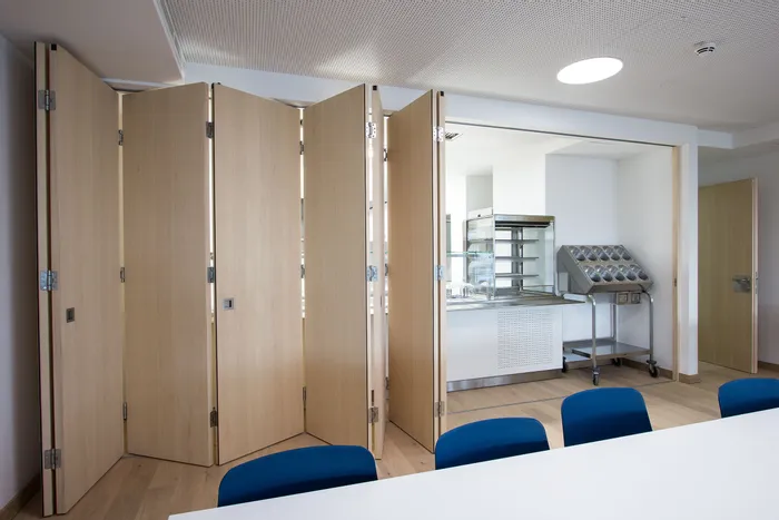 Faltbare Trennwand aus Holz in modernem Konferenzraum mit Blick auf Küchenbereich