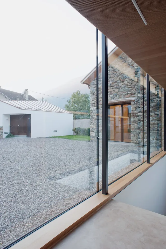 Modernes Haus mit großen Glasfenstern und Blick auf Kieshof und Steingebäude