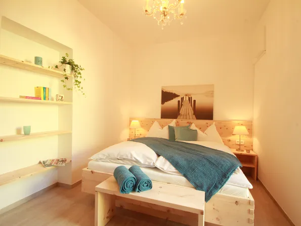 Helles Schlafzimmer mit Holzbett, blauer Decke, Nachttischen und Regalwand
