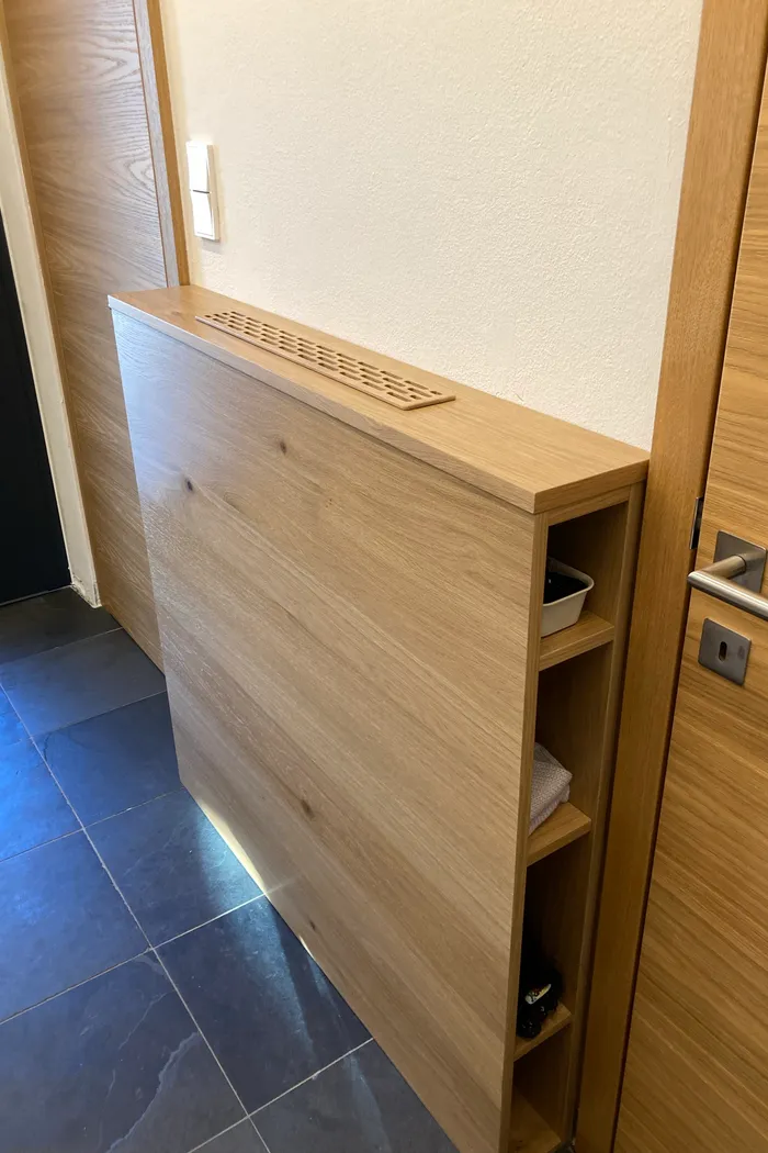 Moderner Holzverkleideter Heizkörper mit seitlichem Regal im Flur auf dunklem Fliesenboden