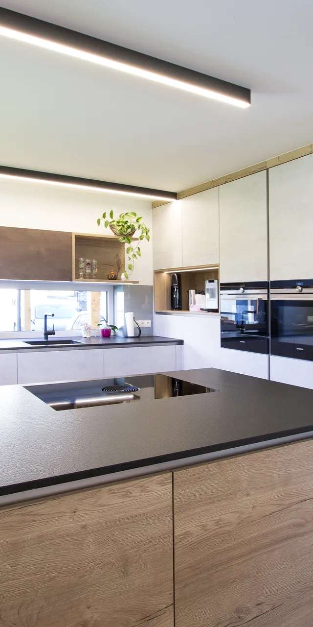 Moderne Einbauküche mit Kochinsel, Holzfronten, schwarzen Geräten und Pflanzen