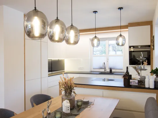 Moderne offene Küche mit weißen Schränken, Hängelampen und Esstisch aus Holz