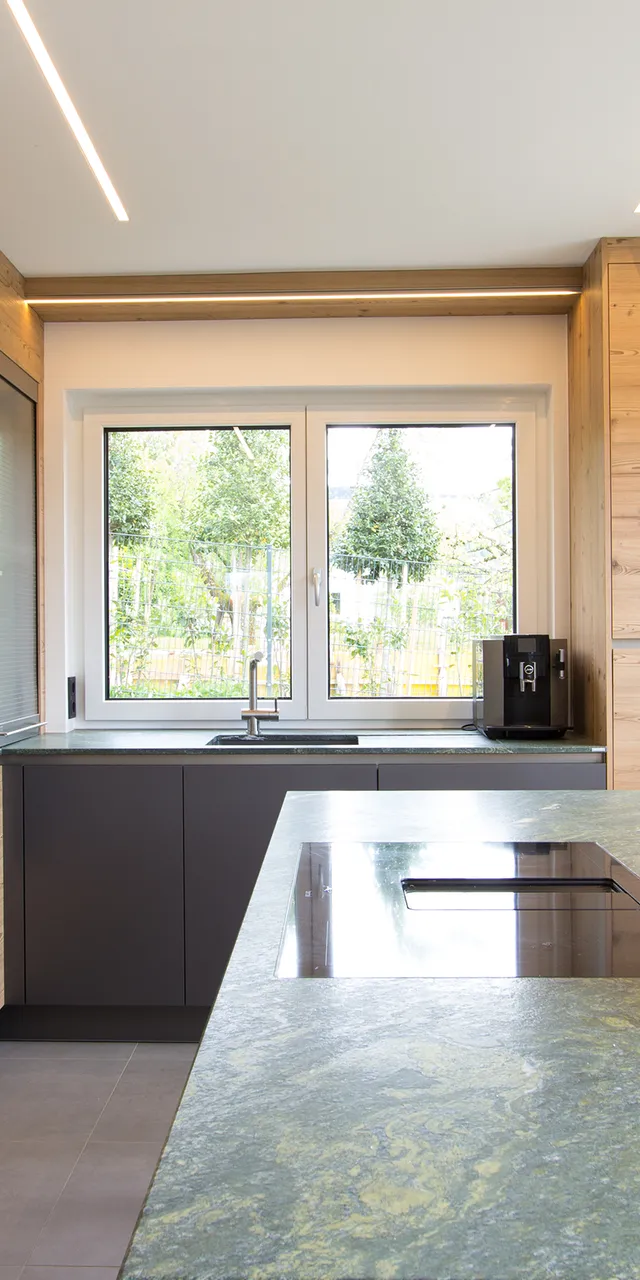 Moderne Küche mit grüner Marmor-Arbeitsplatte, Holzfronten und Schüssel mit Obst auf der Insel