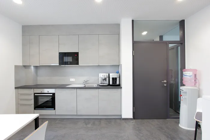 Moderne Büroküche mit grauen Schränken, Kaffeemaschinen und Wasserautomat