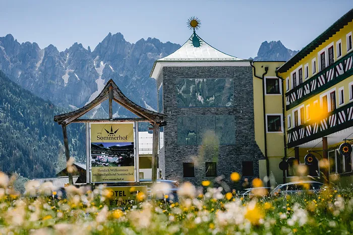 Hotel Sommerhof in den österreichischen Alpen mit Blumenwiese und Gebirgskulisse im Hintergrund