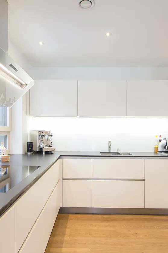 Moderne weiße Einbauküche mit Kochfeld, Dunstabzugshaube und Holzfußboden