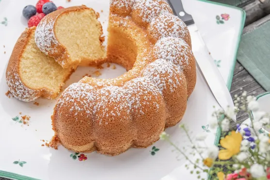 Frisch gebackener Gugelhupf mit Puderzucker auf Teller mit Beeren und Messer serviert