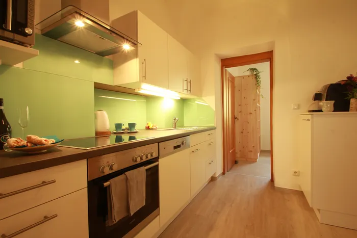 Moderne Küche mit grüner Glasrückwand, Einbaugeräten und hellem Holzfußboden