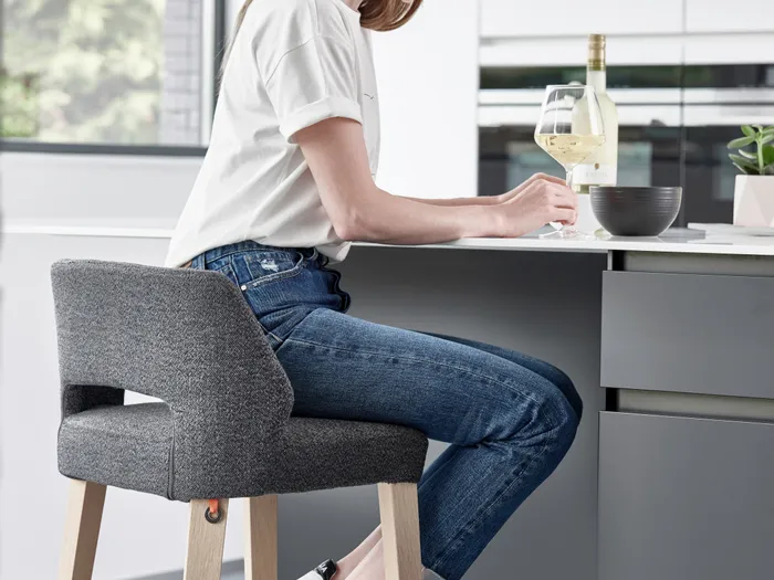Frau sitzt auf modernem Barhocker in heller Küche mit Weinglas und Schüssel auf dem Tresen