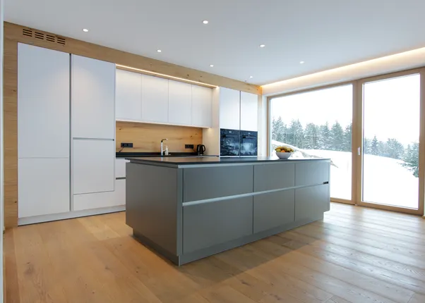 Moderne Einbauküche mit Kochinsel, Holzfußboden und Panoramafenster mit Blick auf verschneite Landschaft