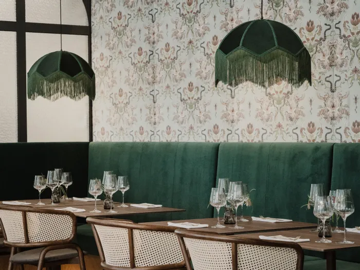Elegantes Restaurant mit grüner Samtbank, Holztischen und hängenden Retro-Lampen