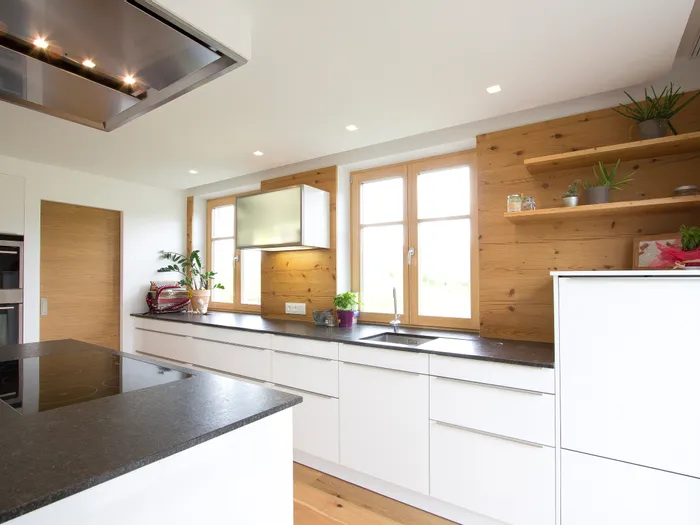 Moderne helle Küche mit weißen Schränken, Holzverkleidung und großen Fenstern