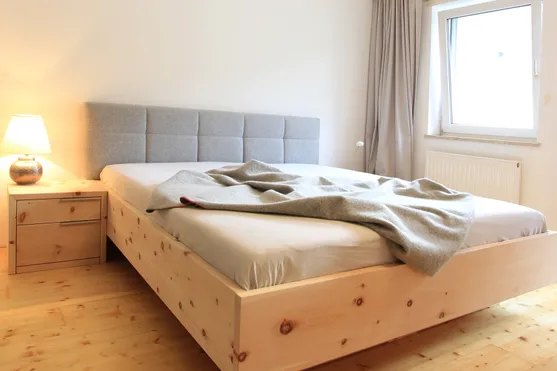 Modernes Schlafzimmer mit Holzbett, grauem Kopfteil und Nachttischlampe auf Holzfußboden