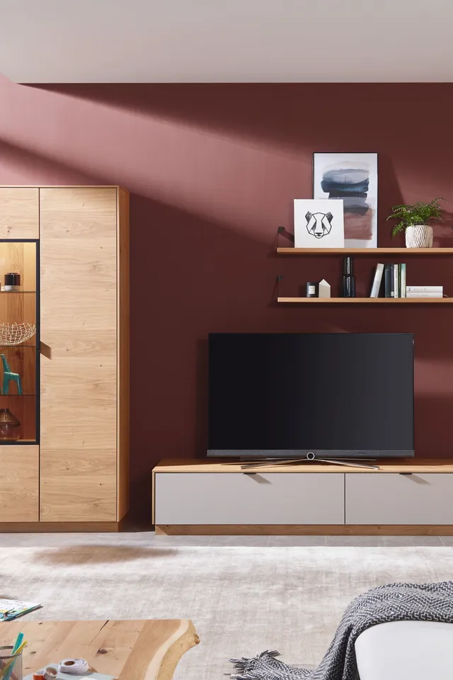 Modernes Wohnzimmer mit Holz- und Hochglanzmöbeln vor bordeauxroter Wand und Flachbildfernseher
