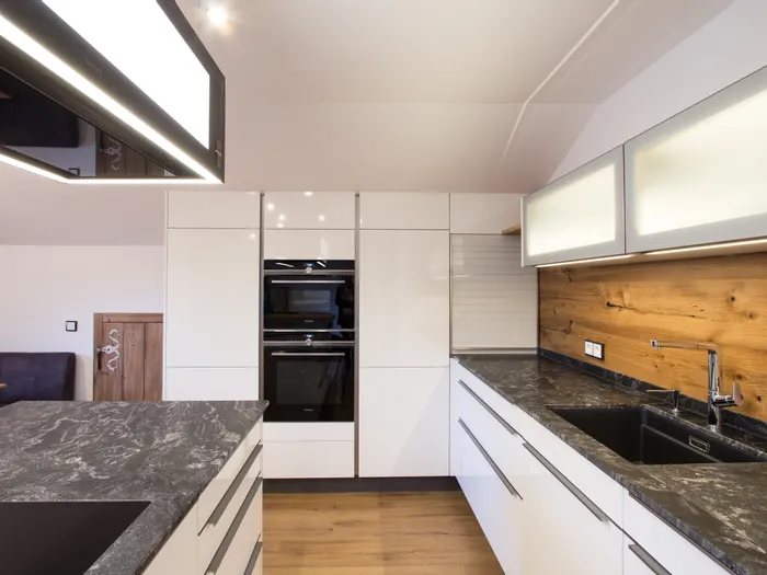 Moderne Einbauküche mit weißen Hochglanzfronten und schwarzer Marmorarbeitsplatte