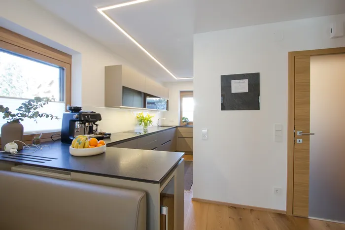 Moderne Küche mit LED-Deckenbeleuchtung, Kaffeemaschine und Obstschale auf der Arbeitsplatte