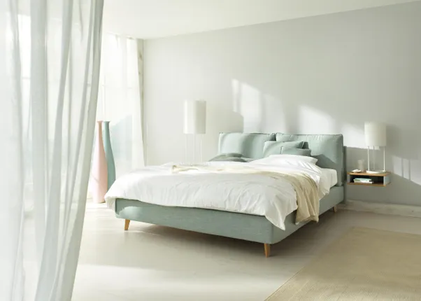 Modernes Schlafzimmer mit hellblauem Polsterbett und natürlichem Lichteinfall