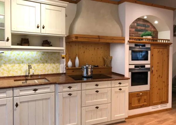 Landhausküche mit weißen Schränken, Holzdetails, Backofen und moderner Kochplatte