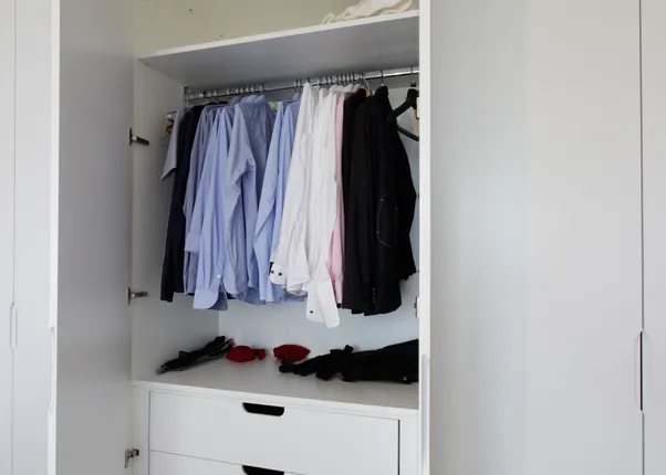 Offener weißer Kleiderschrank mit Hemden, Anzügen und Schubladen in modernem Schlafzimmer